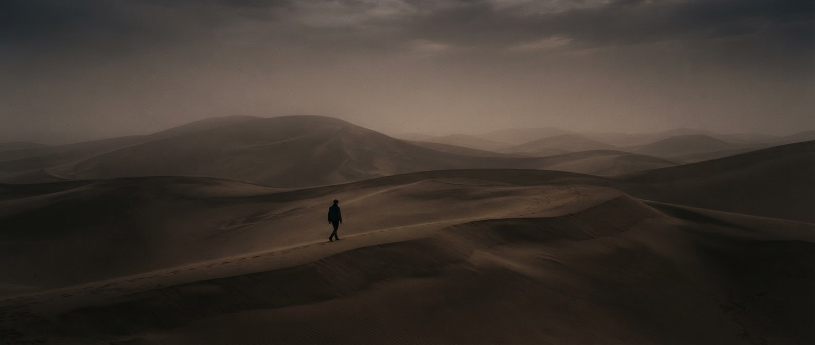 Vaste paysage de dunes brumeuses au crépuscule avec une silhouette lointaine