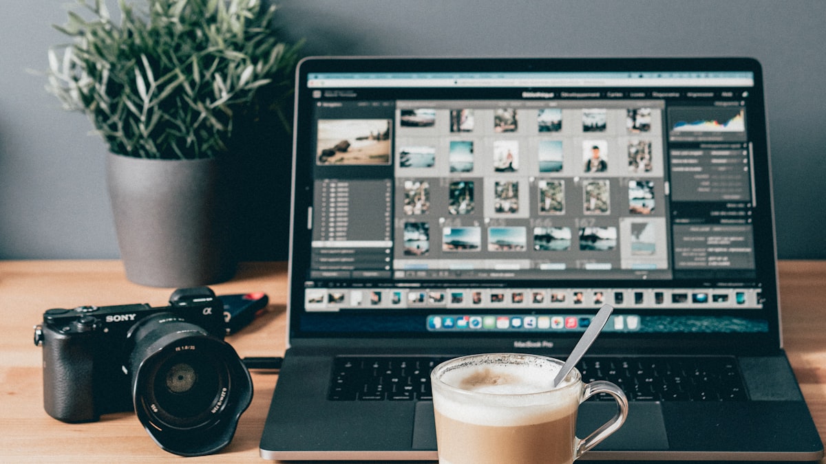 Ordinateur portable ouvert sur un logiciel de retouche photo, appareil photo et plante sur un bureau en bois